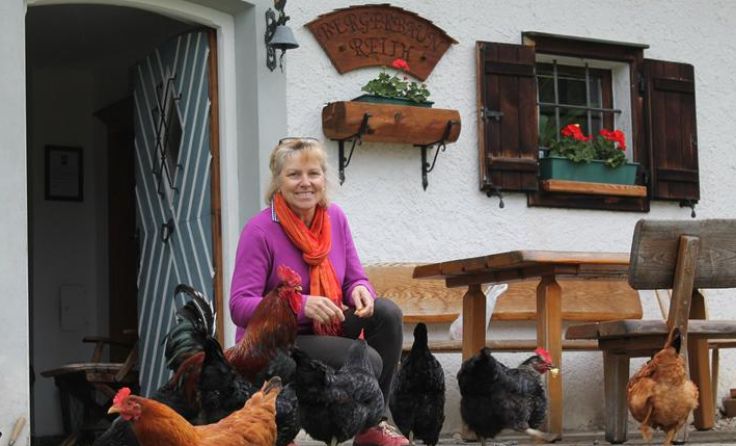 Die Ortsbäuerin mit ein paar Hühnern und dem Hahn vor der Almhütte